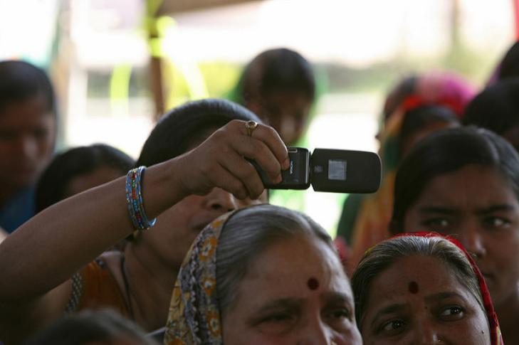 Photo: Woman takes photo with cellphone at a community meeting. Simone D. McCourtie/World Bank via Flickr